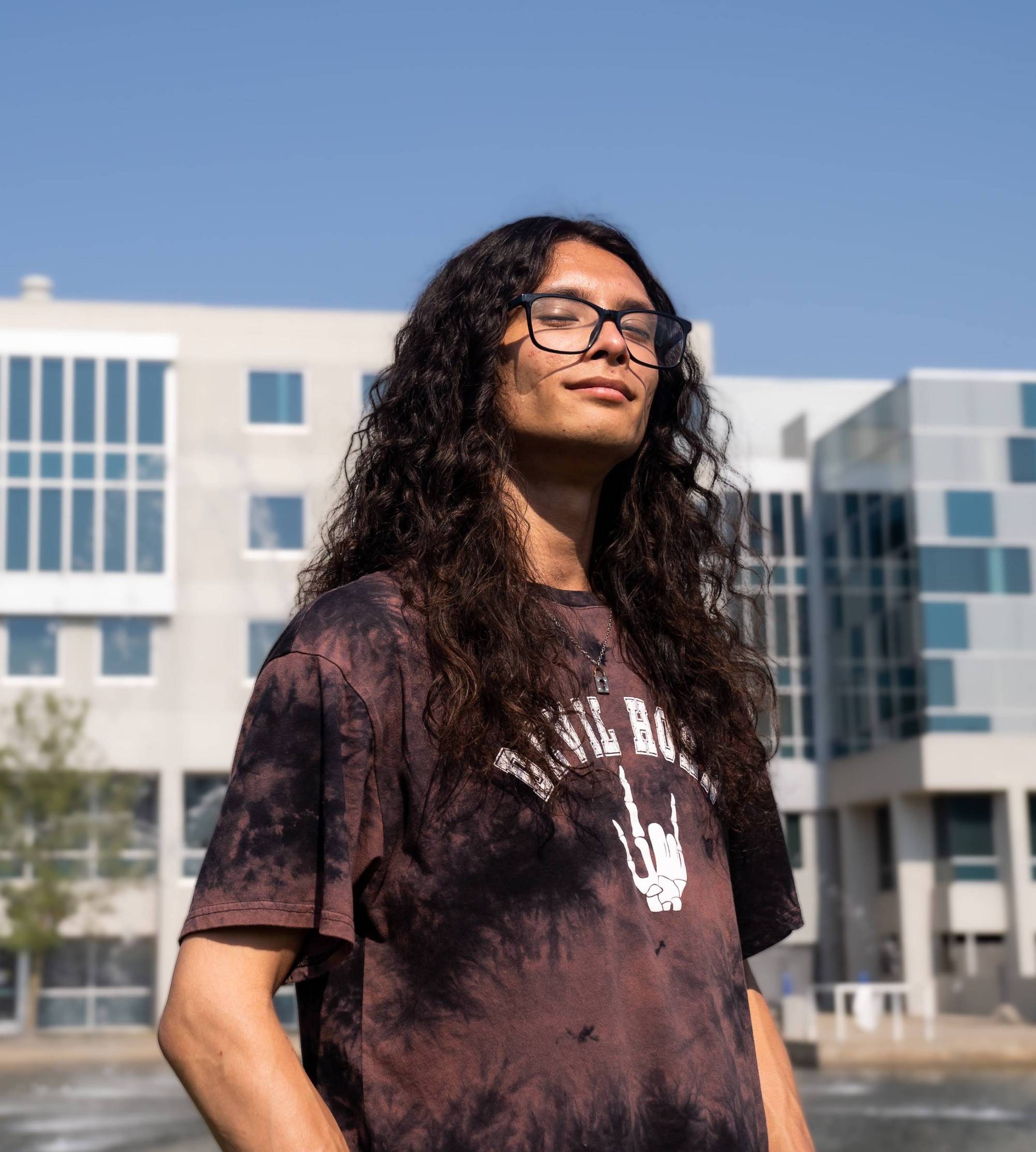 Student with long, curly brown hair standing in front of grey building
